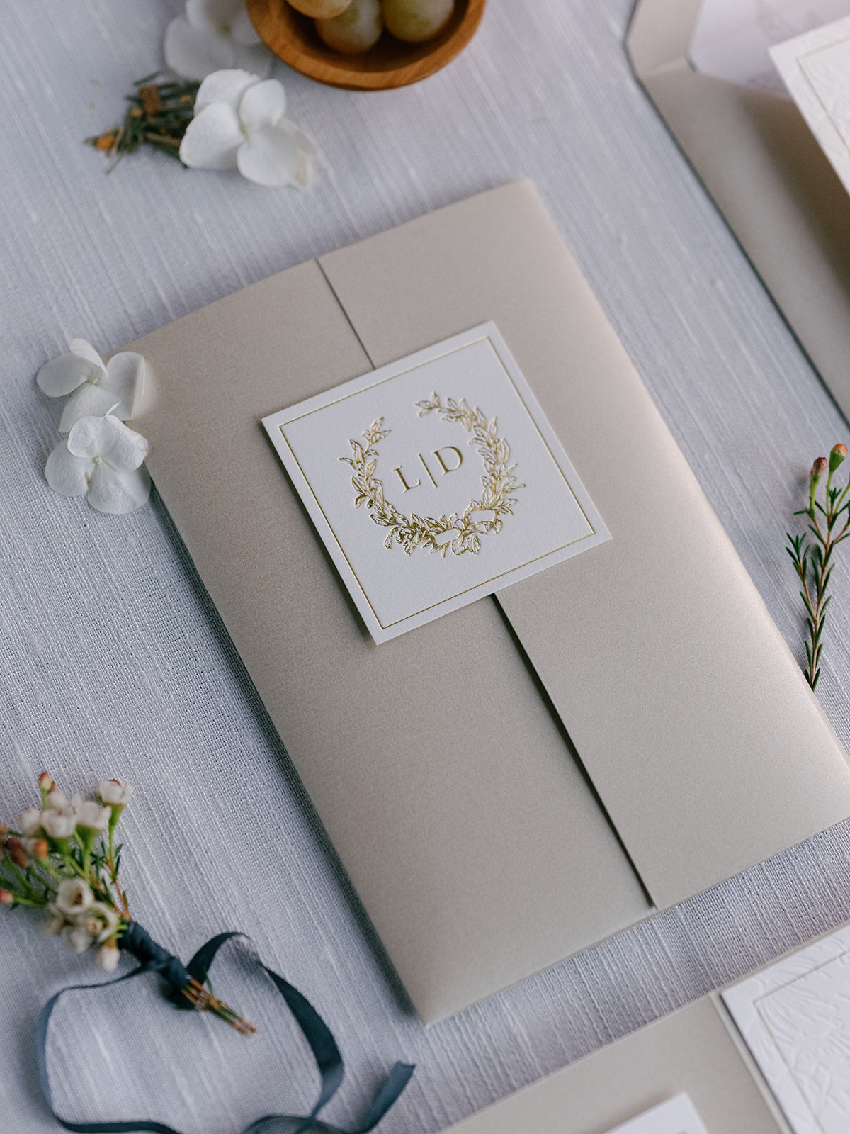 Beige invitation box with a card featuring 'LID' design on a light gray surface with floral decorations.