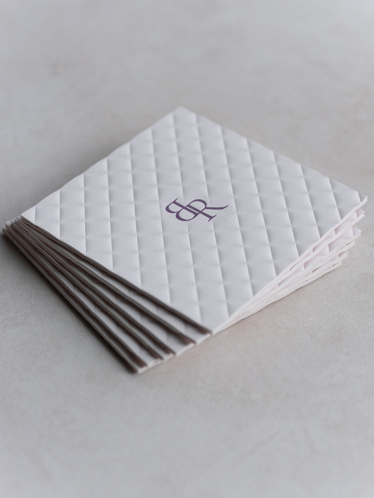 Stack of white quilted napkins with a monogram on a light gray background