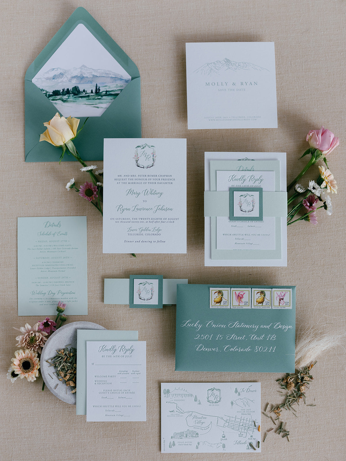 Wedding invitation suite with envelopes and cards on a textured surface with flowers.