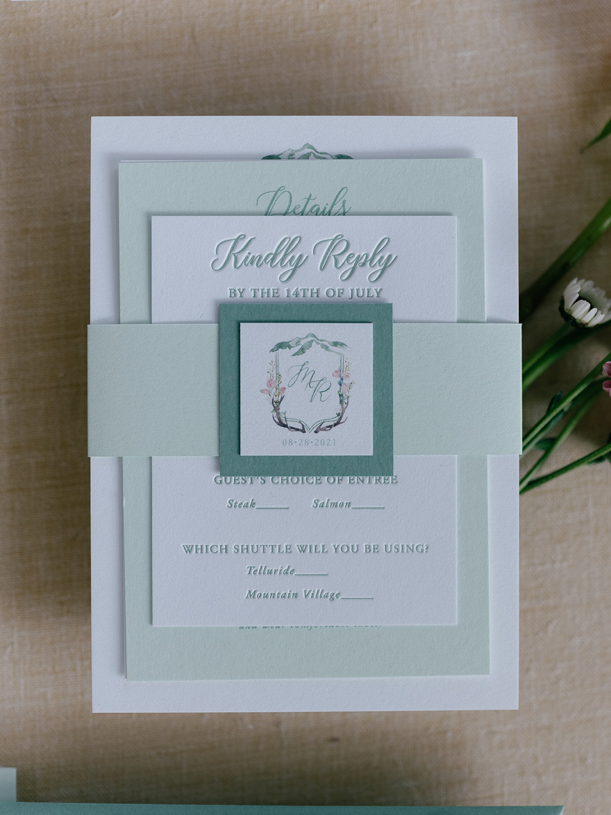 Wedding invitation set with green accents on a wooden surface